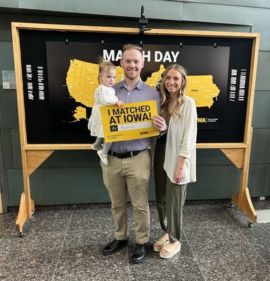 Marshall Rupe with his wife and daughter. They stand in front of a map of the United States and he holds a sign that says, "I Matched at Iowa in Psychiatry."